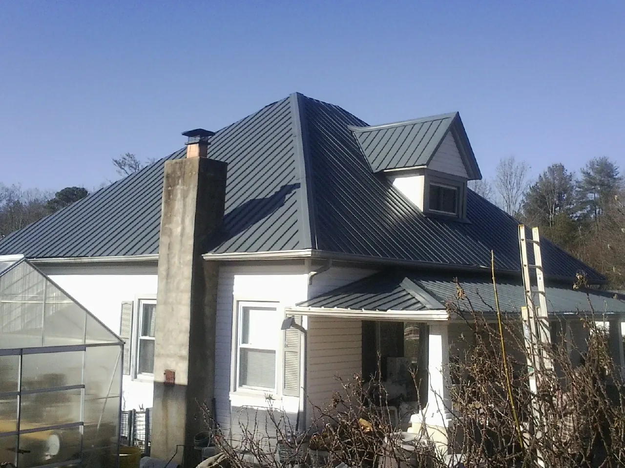 Dark blue standing seam metal roof on a white farmhouse with dormer — Slate & Tile Roof Repair by Roofing Brothers in Spiceland