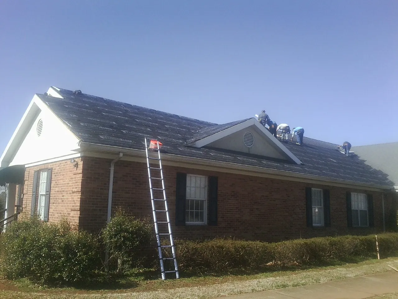 Crew tearing shingles off a brick ranch roof with a ladder set — Metal Roof Repair work by our crew in Spiceland