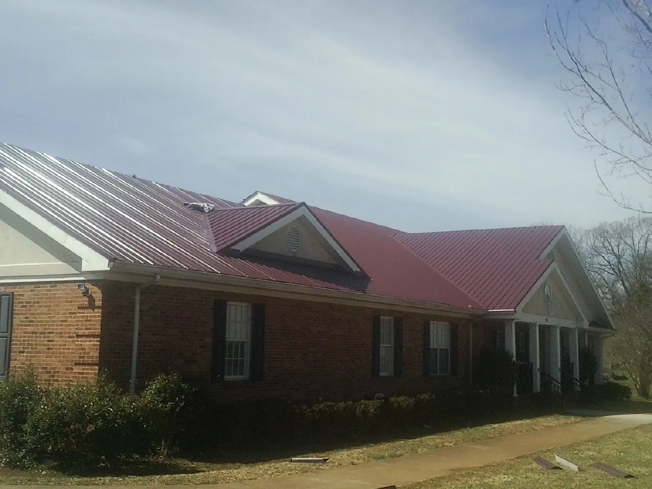 Red metal roof with gabled entries on a long brick building, from a Hail Damage Roof Repair job in Spiceland