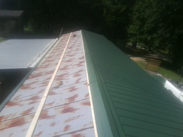 Old rusted panels beside newly installed green metal roofing — Wind Damage Roof Repair by Roofing Brothers in Spiceland