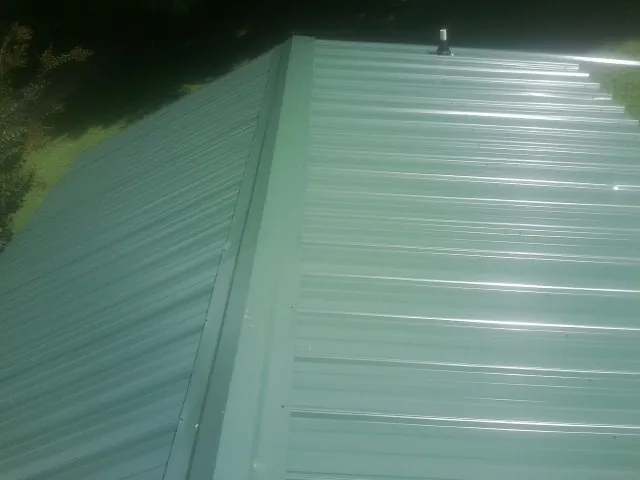 New green metal panels meeting at the ridge of a roof — Flat Roof Repair work by our crew in Spiceland