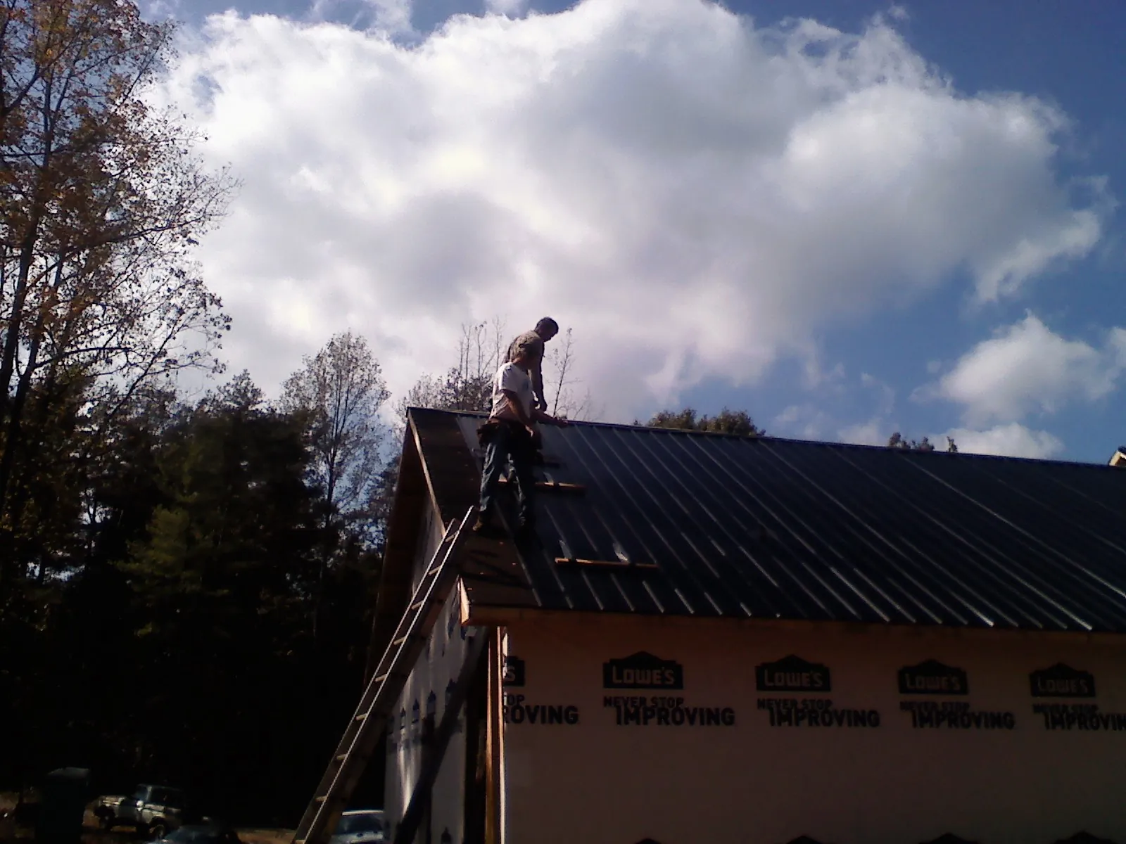 Roofer fastening dark metal panels high against a cloudy sky, from a Roof Inspection job in Spiceland