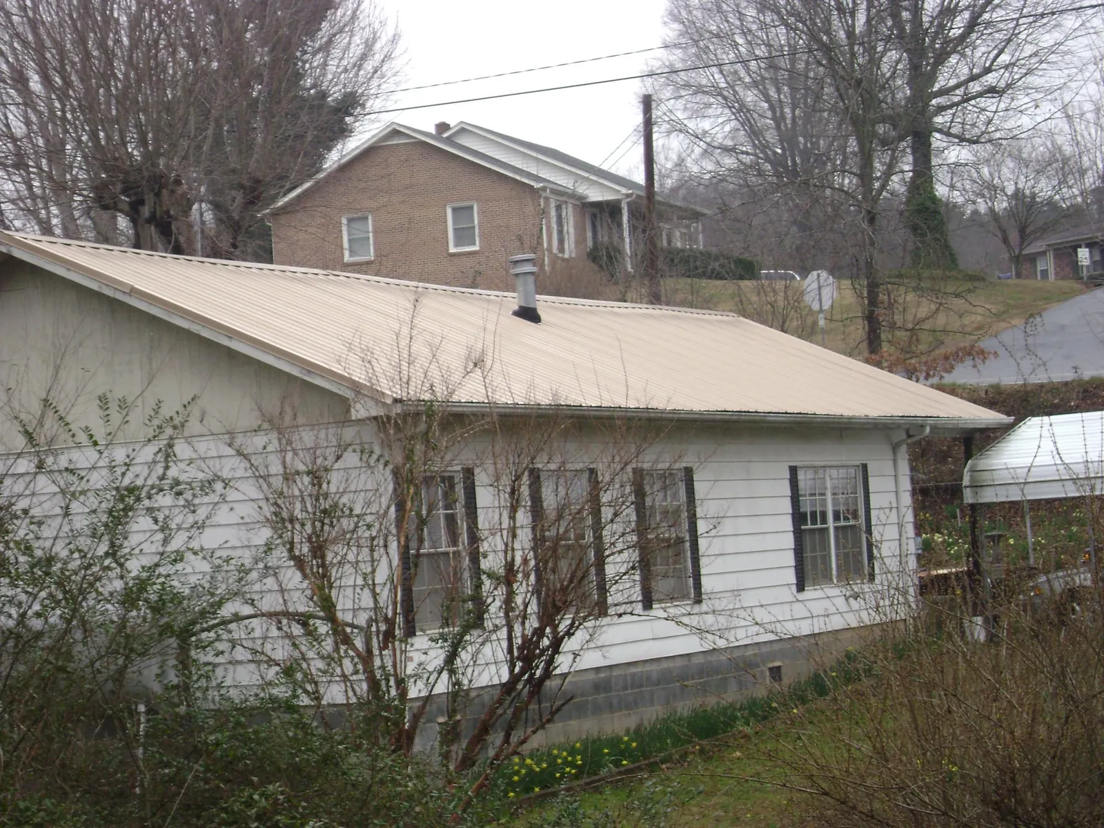 Tan metal roof on a white sided house set into a hillside — Commercial Roofing by Roofing Brothers in Spiceland